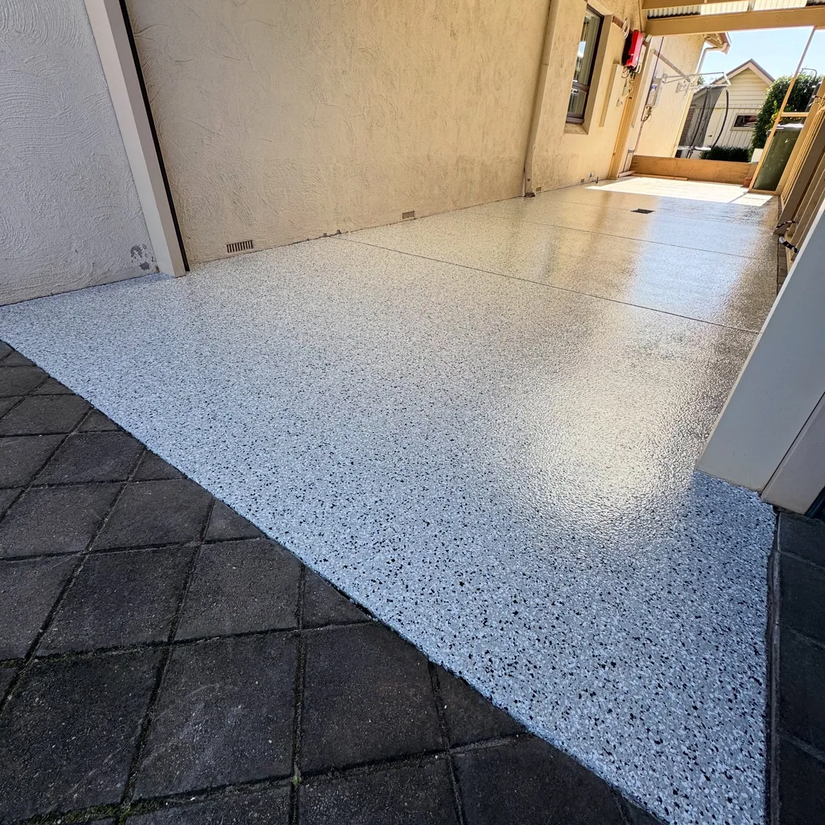 Glossy light grey flake floor in a carport, meeting dark paving at the front