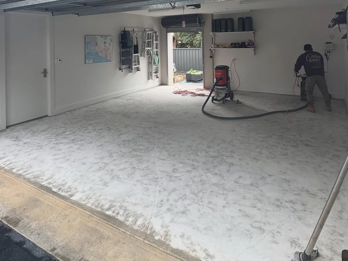 The same garage mid-preparation — slab being ground back with a dust extractor running