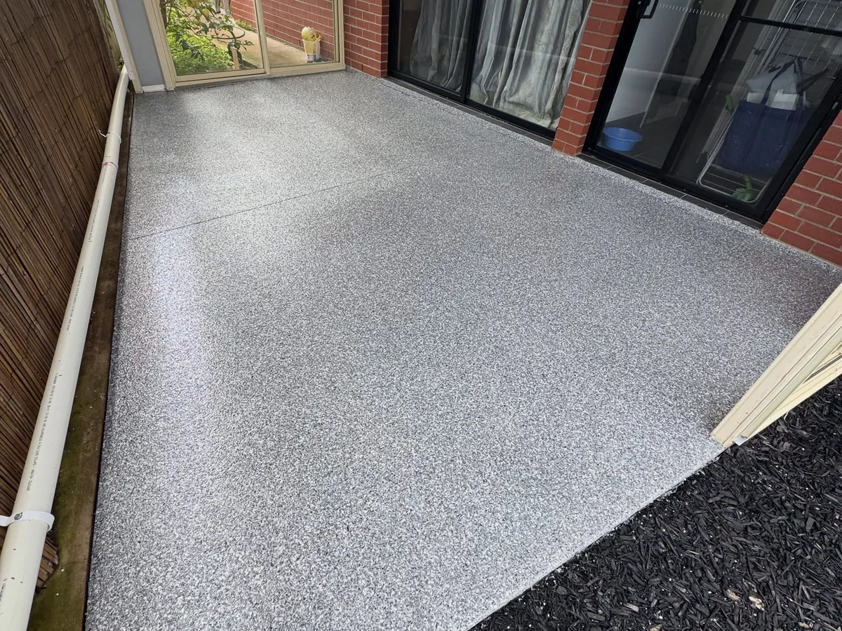 Covered patio after coating — grey flake floor running up to the red-brick wall and sliding doors