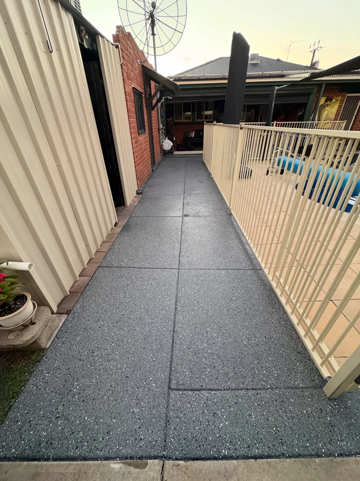 Charcoal flake coated side path running between a shed and the pool fence
