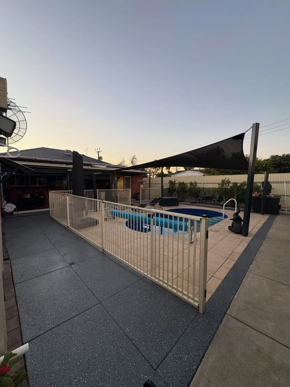 Charcoal flake coated slab wrapping around a fenced backyard pool at dusk